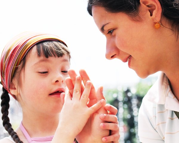 Ein junges Mädchen mit Behinderung reicht einer Betreuerin die Hand | © Caritas München und Oberbayern